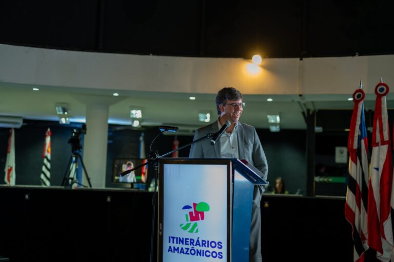 Paulo Andrade, homem, branco, de terno, em um palco de pé, falando ao microfone.