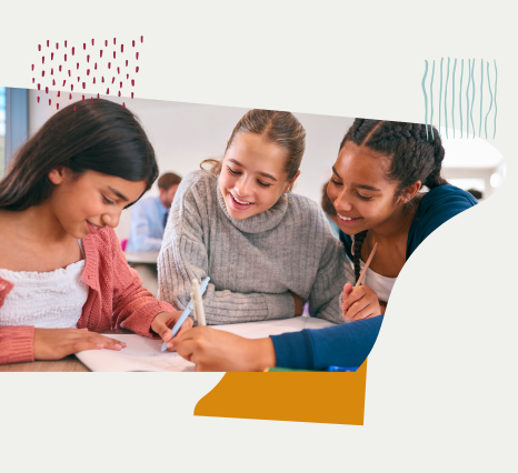 Três meninas, sentadas ao redor de uma mesa, estudando juntas, com um caderno e lápis. 