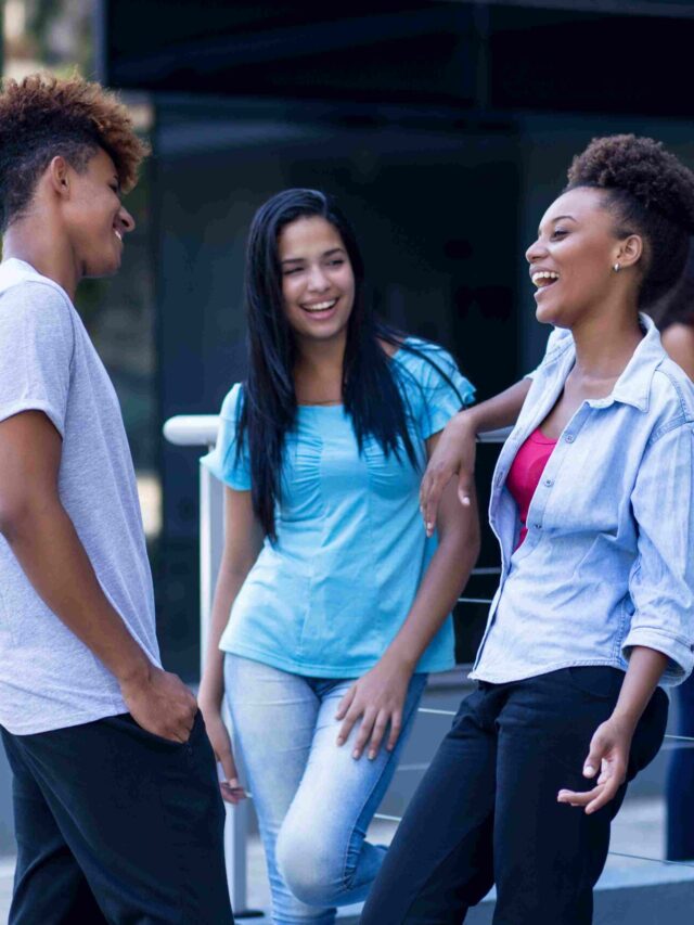 Trio de estudantes conversam em área externa.